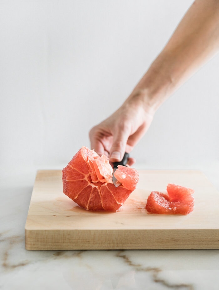hand cutting a segment out of a grapefruit on a wood cutting board.