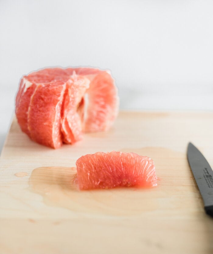 grapefruit segment on a wooden cutting board with a grapefruit behind it.