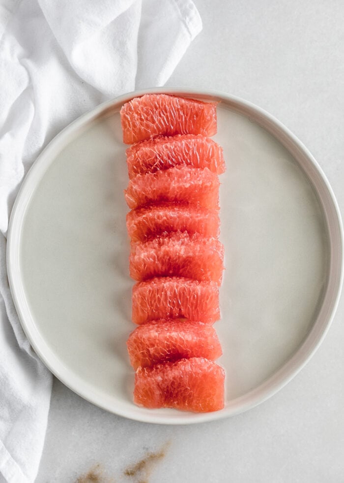 grapefruit segments in a straight line on a white plate. 