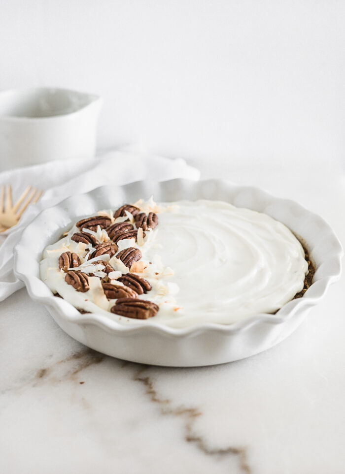 round white baking dish with hummingbird baked oatmeal topped with Greek yogurt frosting and pecans.