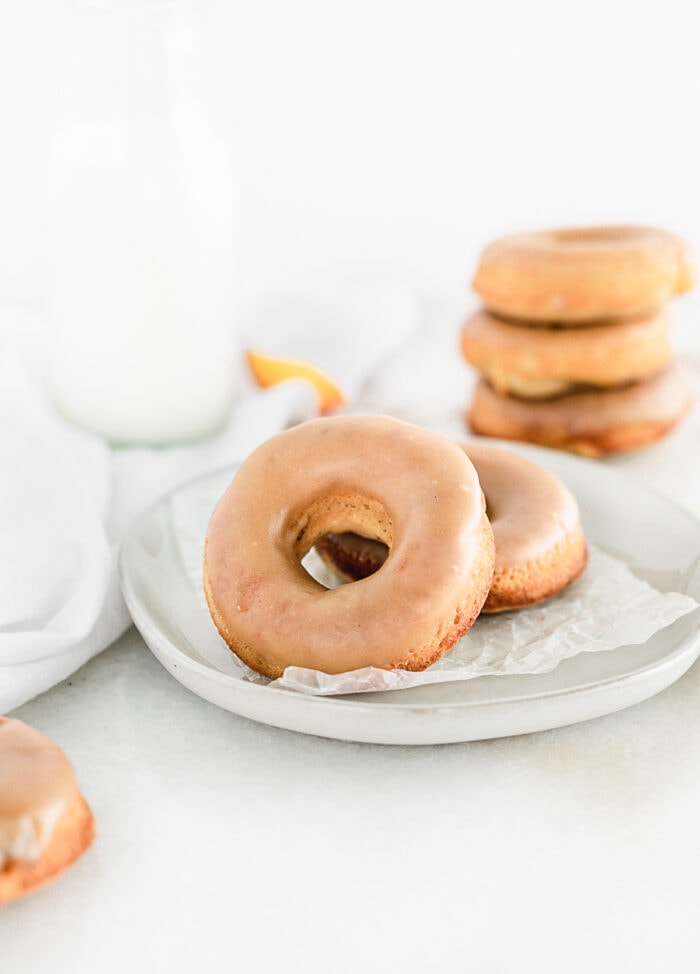 two peach donuts with brown sugar glaze on a plate with a stack of donuts in the background.