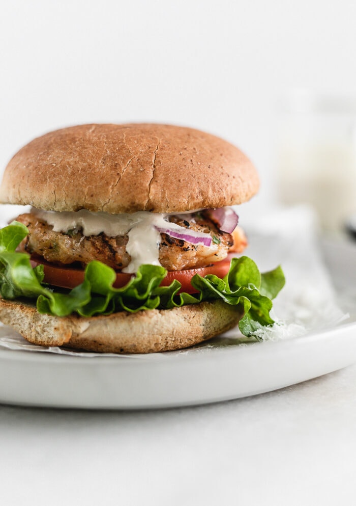 closeup of grilled caesar shrimp burger on a grey plate.