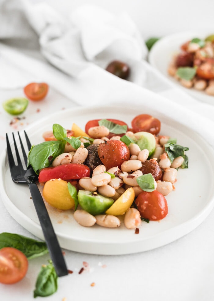 tomato white bean salad on a white plate with a black fork.