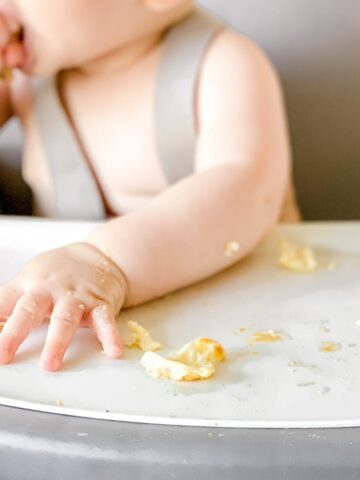 closeup of a baby's hand on a high chair tray with pieces of scrambled egg.