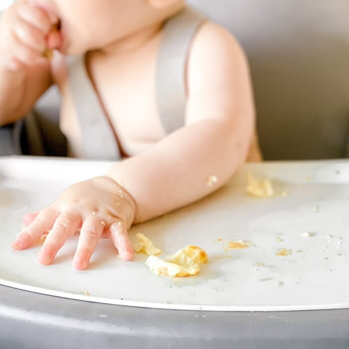 closeup of a baby's hand on a high chair tray with pieces of scrambled egg.
