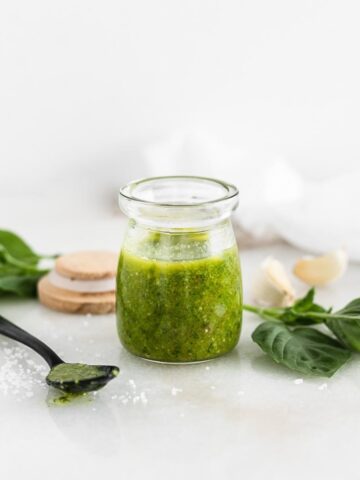 glass jar of basil vinaigrette with a black spoon and basil leaves beside it.