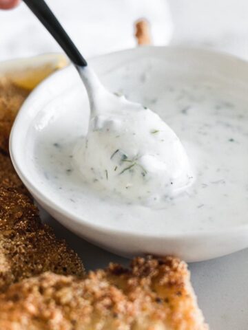 black spoon lifting dill tarter sauce from a small white bowl.