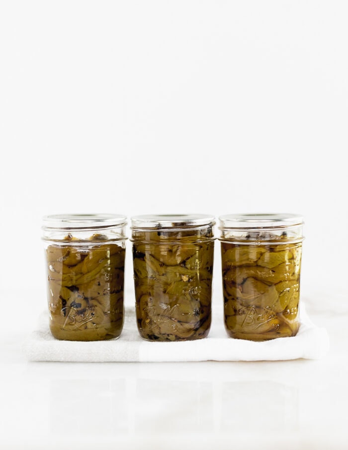 three jars of roasted hatch chiles in a straight line on a white towel.