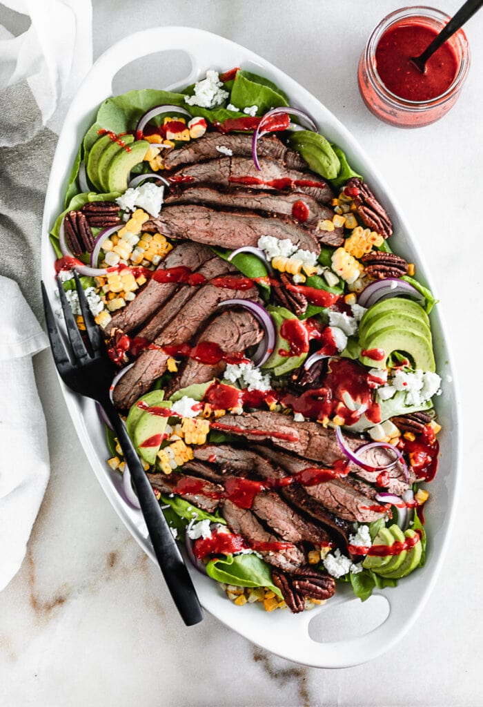 overhead view of raspberry chipotle flank steak salad on a white oval platter with a black serving fork.