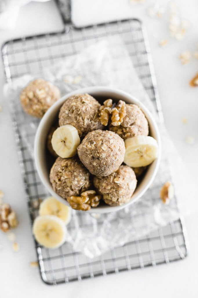 overhead view of banana bread snack balls in a small bowl with banana slices and walnuts.