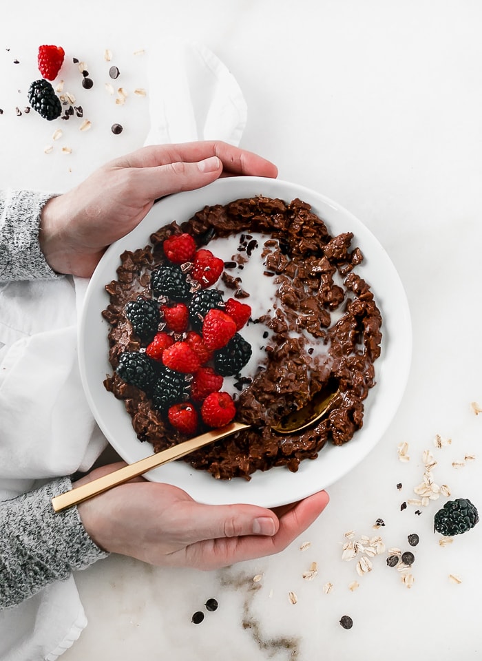 overhead view of hands holding a bowl of chocolate oatmeal topped with berries.