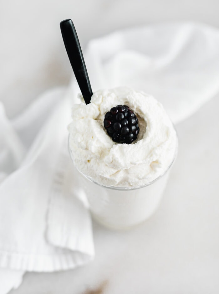 whipped cream in a glass with a blackberry on top and a black spoon in it.