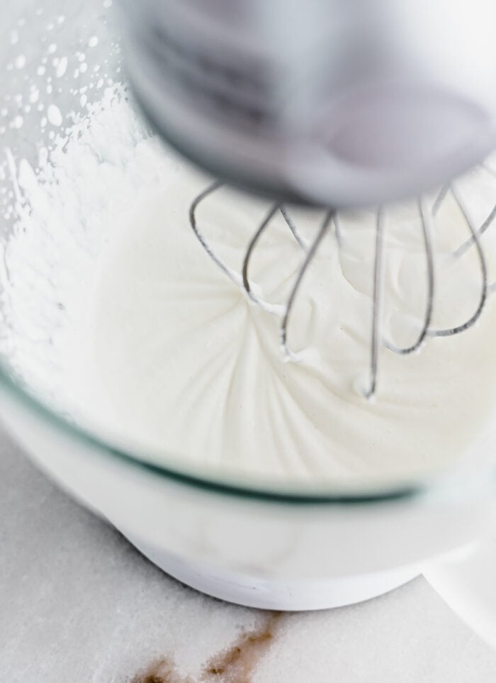 overhead view of whipped cream being whipped in a stand mixer.