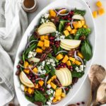 overhead view of pumpkin spinach salad on a white oval serving dish.