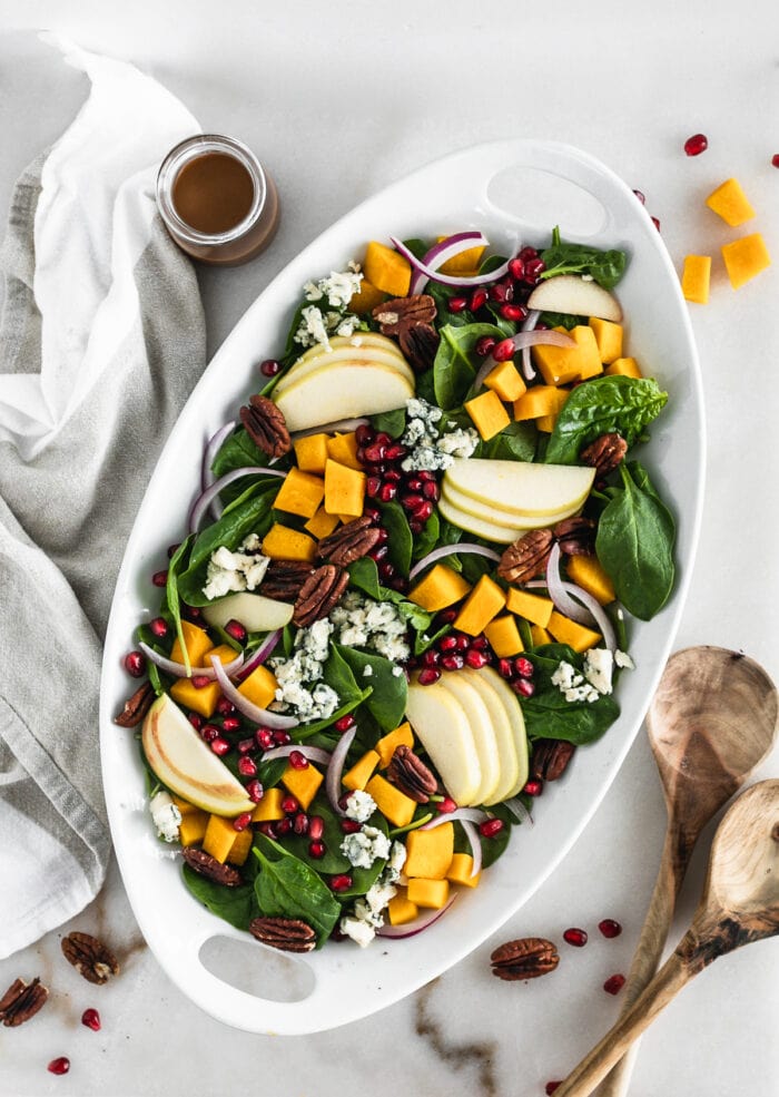 overhead view of pumpkin spinach salad on a white oval serving dish.