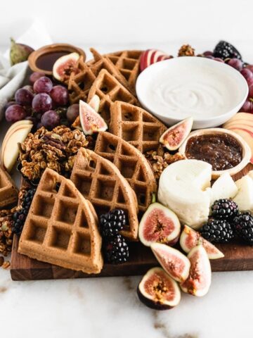 fall brunch board with waffles, yogurt, fruit and cheese on a white marble background.