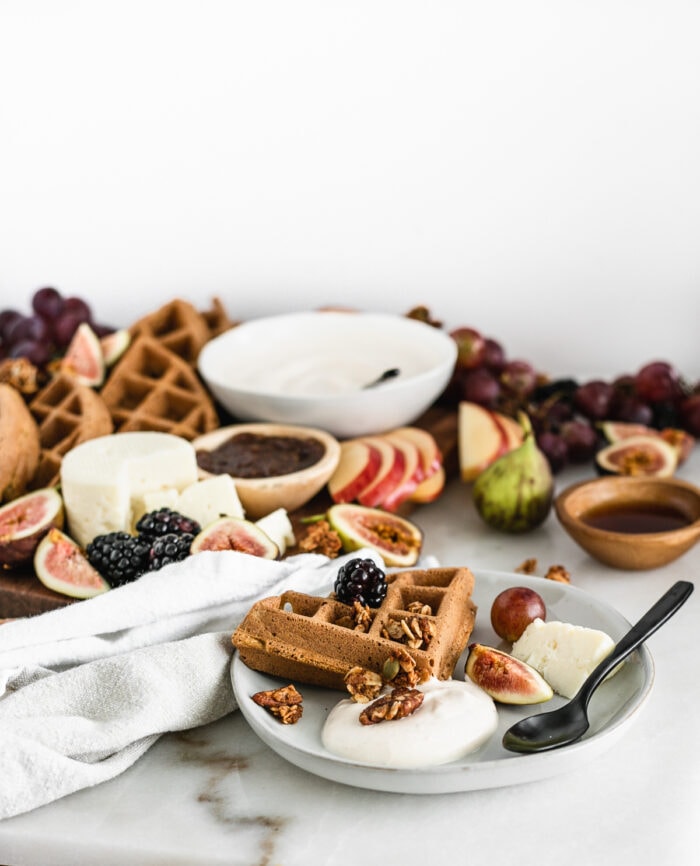 plate with a waffles, yogurt, and fruit with a black spoon in front of a fall brunch board.