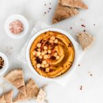 overhead view of a bowl of pumpkin hummus surrounded by pita wedges.