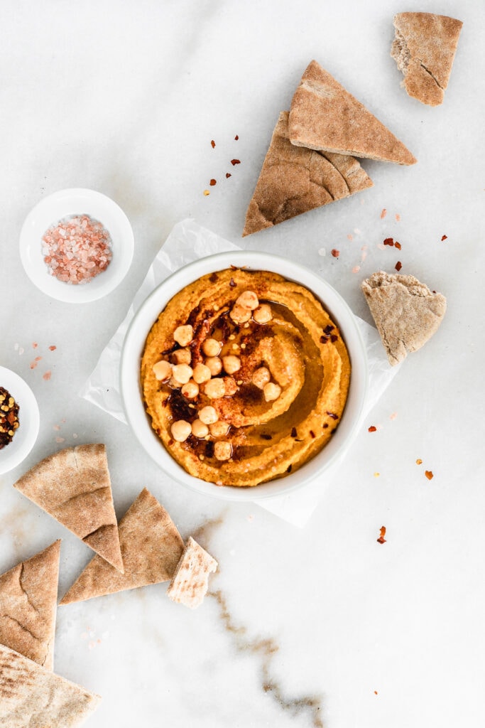 overhead view of a bowl of pumpkin hummus surrounded by pita wedges.