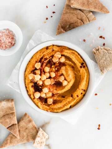 overhead view of a bowl of pumpkin hummus surrounded by pita wedges.