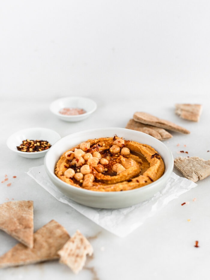 greey bowl of pumpkin hummus tipped with chickpeas surrounded by pita wedges.