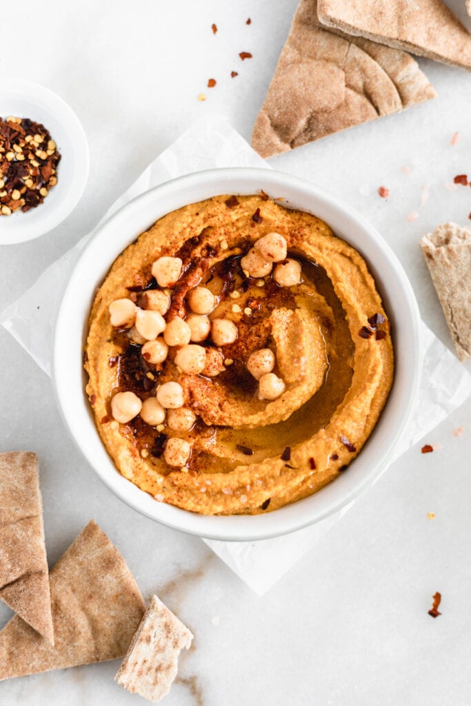 overhead view of a bowl of pumpkin hummus surrounded by pita wedges.