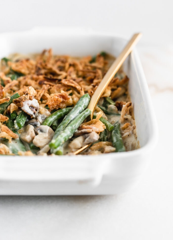 closeup of a spoon of green beans from green bean casserole sitting on top of a white dish of casserole.
