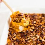 gold spoon lifting pecan sweet potato casserole out of a white dish.