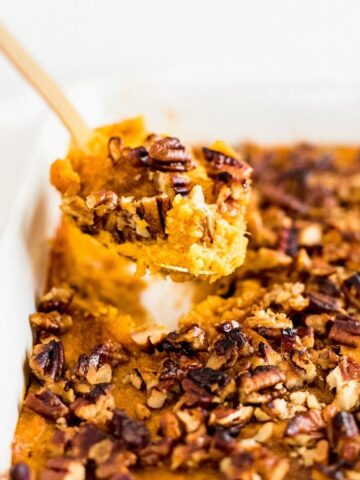 gold spoon lifting pecan sweet potato casserole out of a white dish.