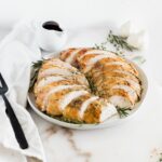 sliced herb roasted turkey breast on a grey platter garnished with fresh herbs.