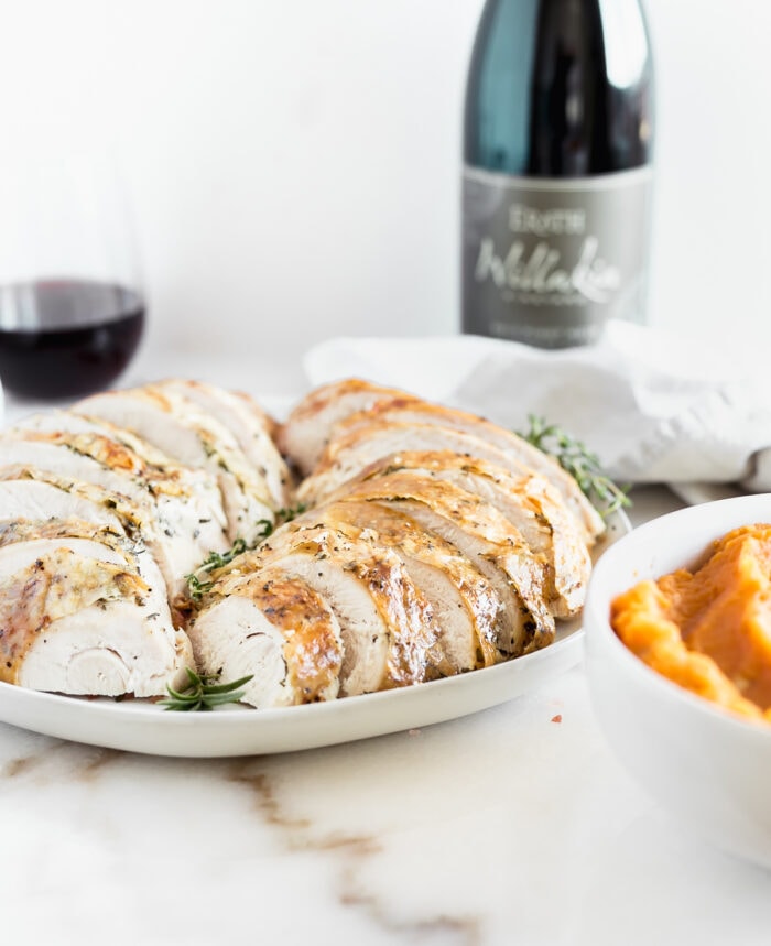 sliced herb roasted turkey breast with a bottle and glass of wine in the background.