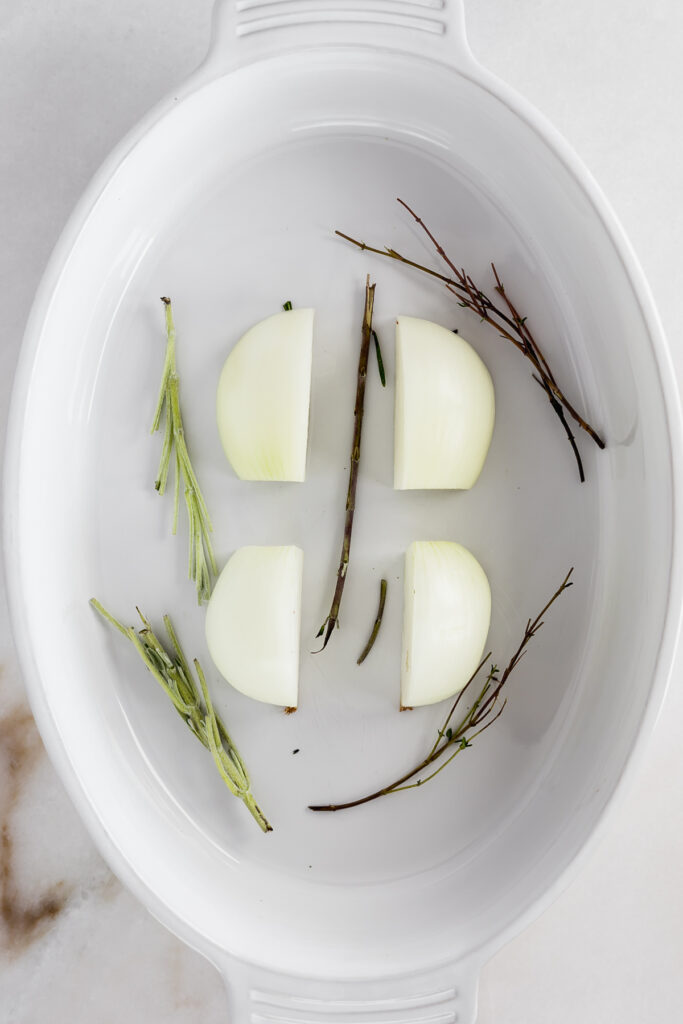 white baking dish with a quartered onion and herb stems in the bottom.