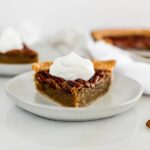 slice of pecan pie on a grey plate topped with whipped cream.