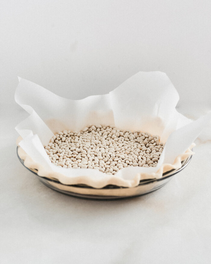 unbaked pie crust in a pie dish with parchment and dry beans in it.