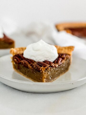 slice of pecan pie on a grey plate topped with whipped cream.