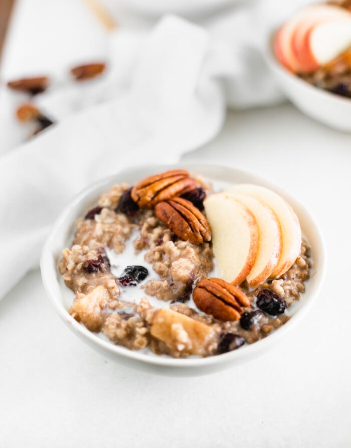 bowl of apple cranberry oatmeal topped iwth apple slices and pecans.