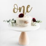 smash cake topped with flowers on a white cake stand.