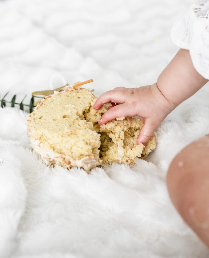 baby hand grabbing a smashed vanilla cake.