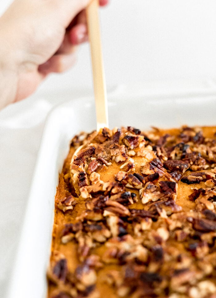 gold spoon digging into sweet potato casserole topped with pecans.