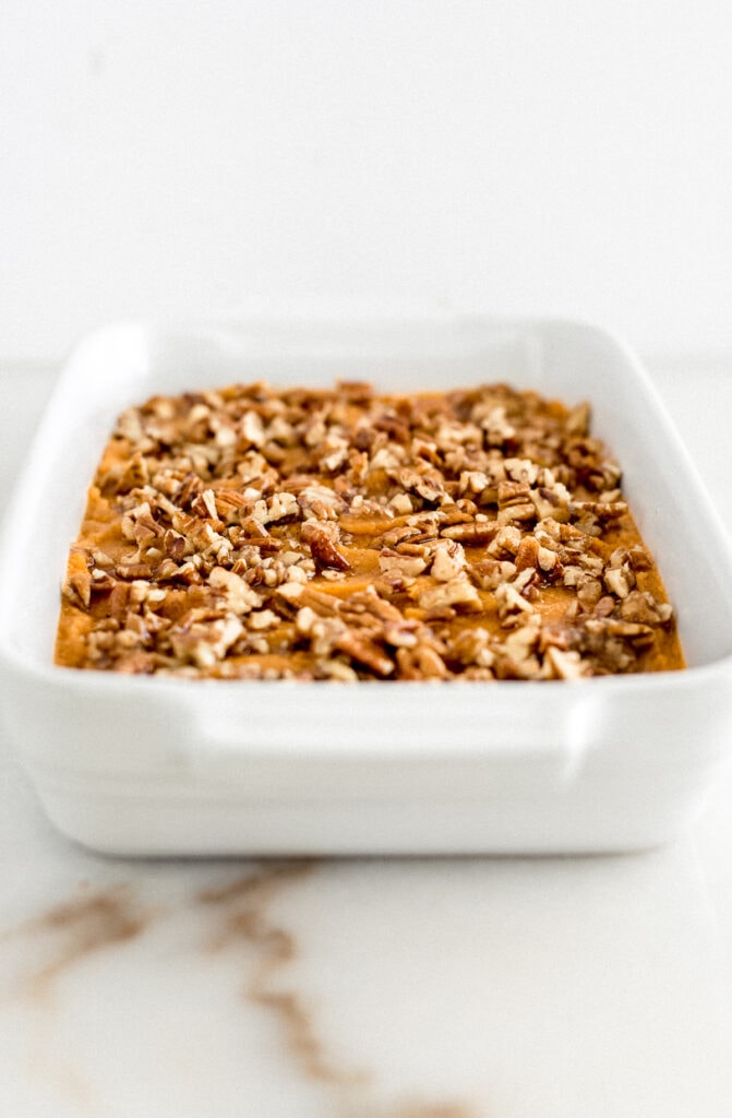 sweet potato casserole with pecan topping in a white dish before baking.