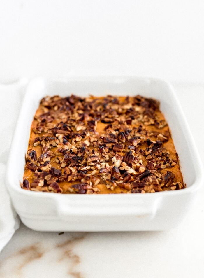 baked sweet potato casserole with pecan topping in a white baking dish.