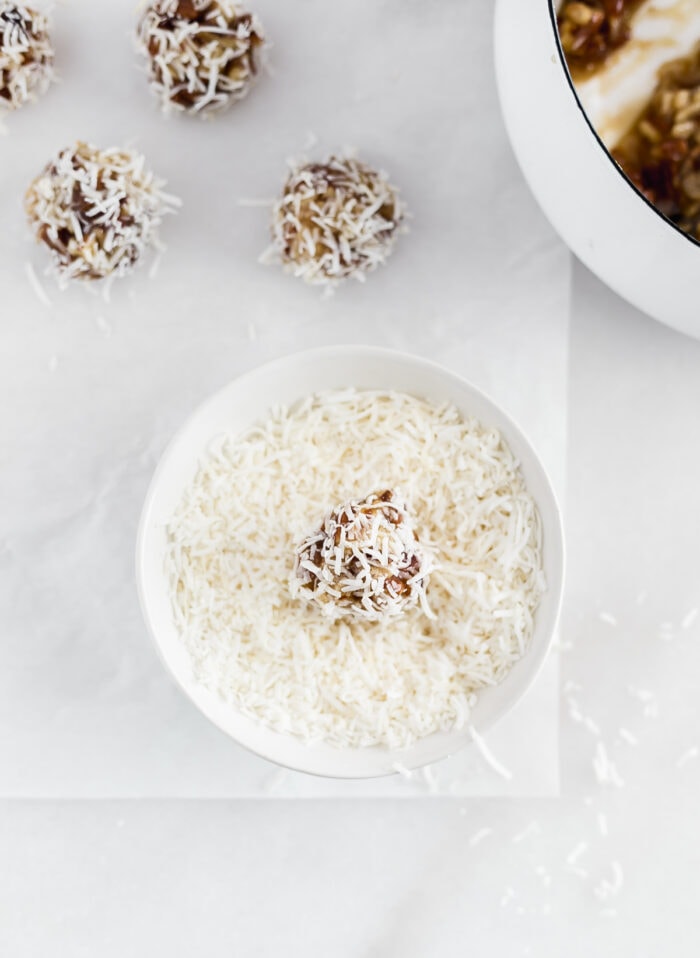 no bake coconut date ball being rolled in coconut.