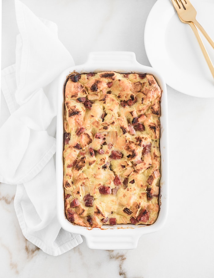 overhead view of ham and swiss strata in a white baking dish on a white background.