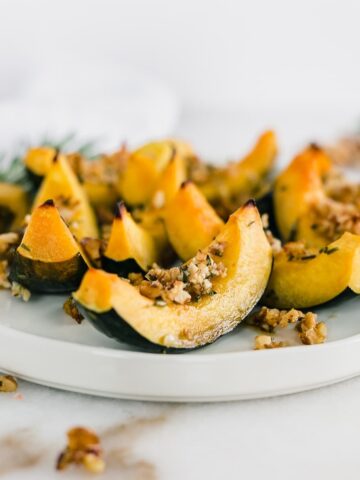 wedges of roasted acorn squash with maple rosemary walnut topping on a white plate.