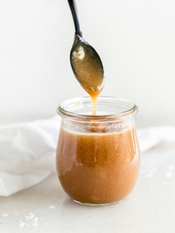 spoon lifting miso caramel sauce out of a glass jar.