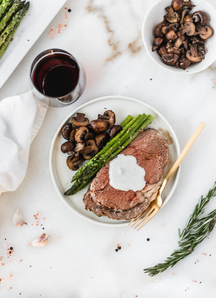 overhead view of prime rib on a plate with asparagus and mushrooms and a gold fork.