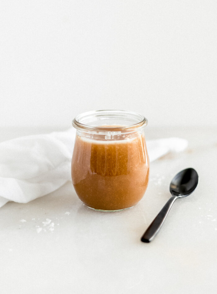 salted miso caramel in a glass jar with a black spoon beside it.