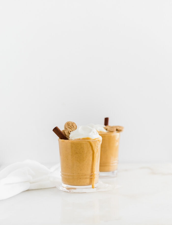 two sweet potato gingerbread smoothies topped with whipped cream, cinnamon sticks, and gingerbread men with a drip running down one glass.