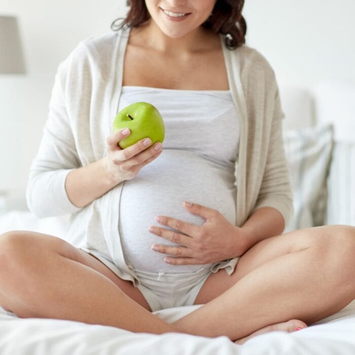 pregnant woman sitting cross legged holding an apple.