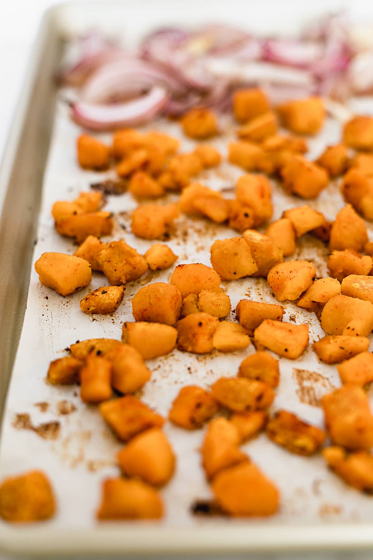 roasted sweet potato cubes and red onion on a baking sheet.